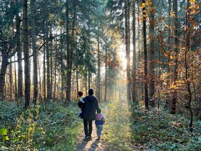Vater mit zwei kleinen Kindern geht durch einen sonnigen Herbstwald