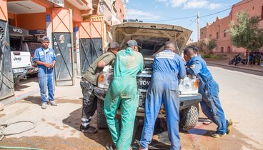 Männer in Arbeitsoveralls sind über ein Auto gebeugt