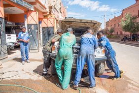 Männer in Arbeitsoveralls sind über ein Auto gebeugt
