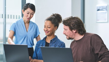 Zwei Mitarbeiter*innen sitzen vor Laptops, während eine dritte etwas erläutert | ©DVV